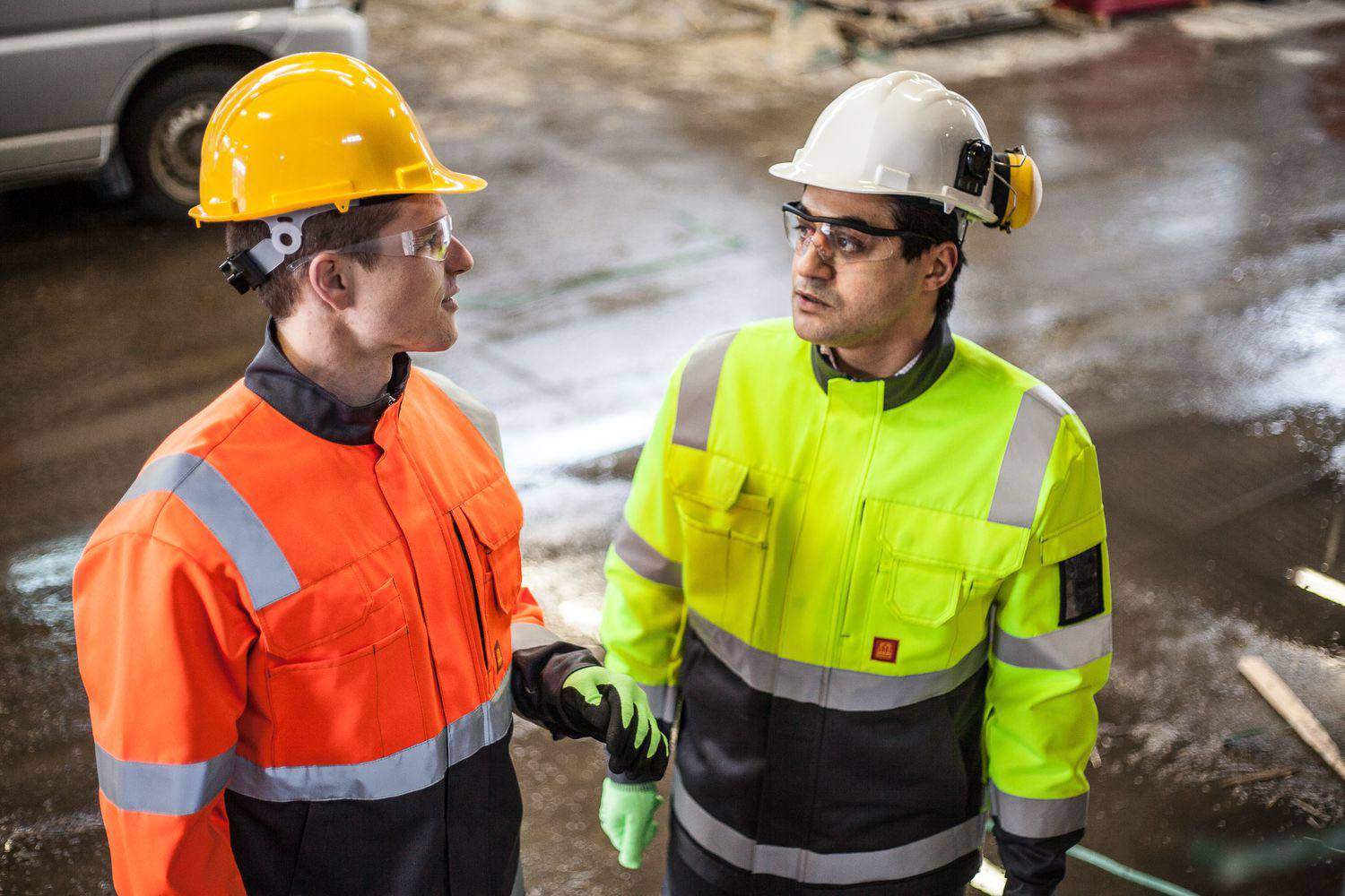 two men wearing hi vis clothing and hard hats looking at each other